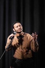 pensive indian comedian performing stand up comedy and telling jokes in microphone on black.
