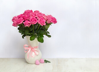 Bouquet pink flowers roses in white porcelain vase and pink hearts on a white table on light background with space for text
