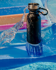Obraz na płótnie Canvas A black insulated bottle on an air mattress with a spray of water hitting it