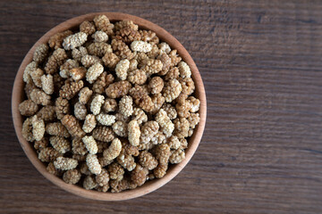 Bowl full of dried mulberry on a wooden background