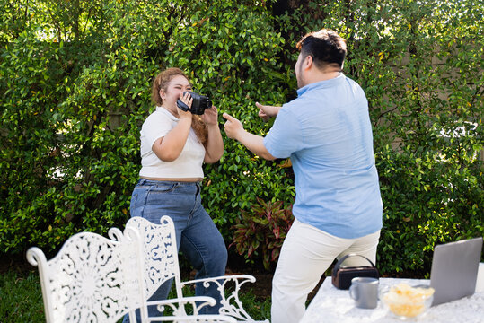Young Asian overweight man and woman dance together at garden while using mobile phone for selfie. confident fat couple enjoyment with music and video camera