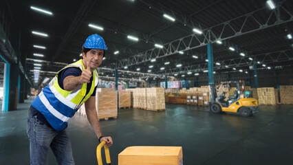 Warehouse worker pulling a pallet truck and taking or upload package box to shelf in large warehouse. Active caucasian man showing thump up and looking at camera with smiling.