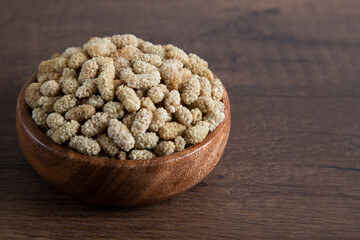 Bowl full of dried mulberry on a wooden background 
