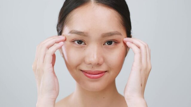 Portrait young Asian woman apply serum and moisturizer on skin around the eyes over grey background.