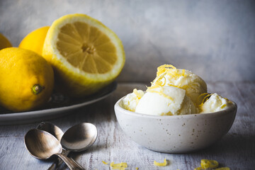 cuenco con helado de limón sobre una mesa de madera blanca, con unas cucharas de postre y un plato de limones detrás