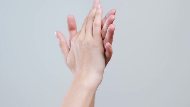 Close up woman applying hand cream and lotion over grey background.