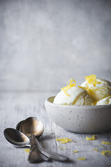 cuenco con bolas de helado de limón y unas cucharillas al lado, sobre una mesa de madera blanca...
