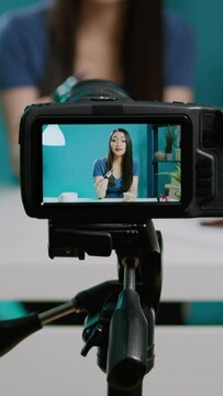 Vertical video: Social media blogger filming product review with camera in studio, using professional streaming equipment. Female vlogger recommending lipstick cosmetics for beauty tutorial on channel