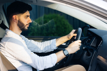 Businessman holding steering wheel while driving modern electric car on the street road. Confident man driving expensive car. Driver Turning Steering Wheel In Luxurious Auto On Trip