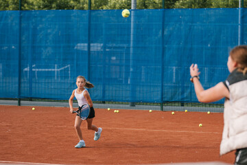 Young girl practicing hitting a tennis ball on an outdoor tennis court. 