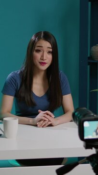 Vertical video: Asian vlogger filming beauty tutorial with smartphone camera, recording makeup video with cosmetics. Beauty influencer streaming online internet broadcast with glam product, videoblog.