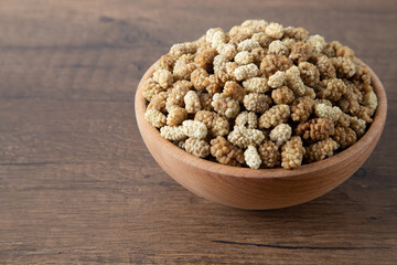 Bowl full of dried mulberry on a wooden background
