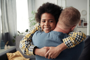Portrait of African happy adoptive boy hugging his foster dad and smiling at camera