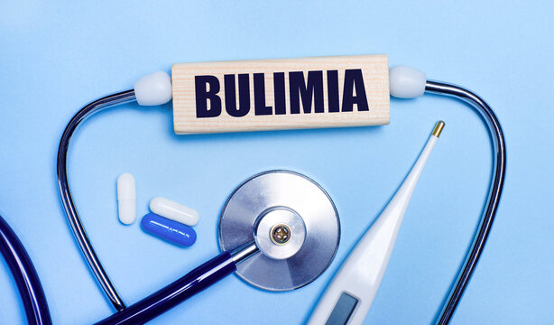 On a light gray background, a stethoscope, an electronic thermometer, pills, a wooden block with the text BULIMIA. Medical concept.