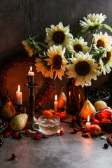 Gently yellow sunflowers on the table with different fruits and berries. Still life in dark lighting with floral arrangement, candles and seasonal fruits.