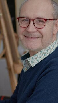Vertical video: Portrait of senior man enjoying art class to develop drawing skills for personal growth. Elder student attending artistic lesson to learn to draw masterpiece on canvas as new years