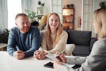 Happy foster couple answering questions from social worker at table during their meeting at home