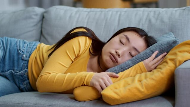 Tired sad young asian woman falling down on sofa at home, resting at domestic interior, close up portrait, slow motion