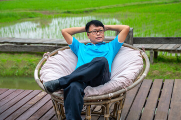 Fototapeta premium Asian man relaxing on a vintage wooden chair in outdoors,Thailand,ASIA.