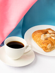 Almond croissant for breakfast on white plate with blue pink  background, flat lay, top view.