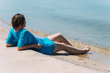 Fototapeta na wymiar Girl in a blue pareo sitting on the beach against sea.