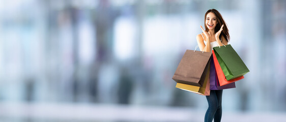 Shopping woman. Happy excited girl, holding many bags, blurred interior or mall background. Copy...