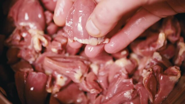 Female Holding and Showing Fresh Raw Peeled Chicken Hearts in Hand. Lots of gutted shiny red chicken hearts, cut into two halves. Dietary meat. By-products of second grade. Food for the poor. Sale.