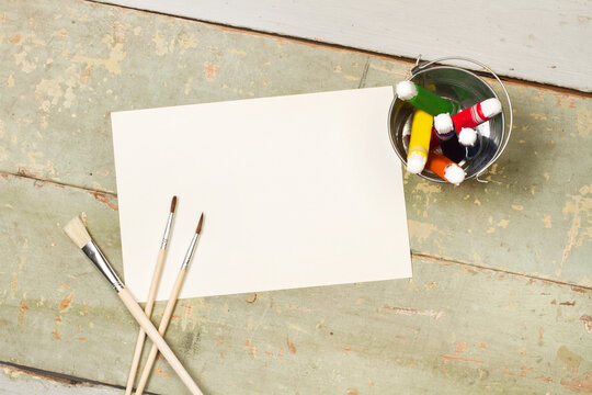 Pinceles y pinturas artisticas junto a un papel en blanco para pintar sobre un fondo de madera r&uacute;stico. Vista superior y de cerca. Copy space