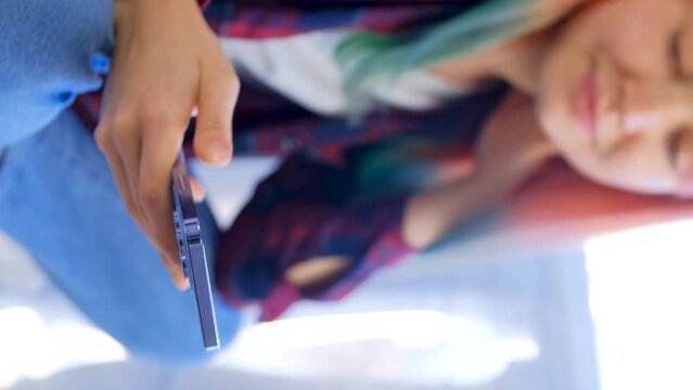 Girl using modern blue mobile phone for communication on social media app. Vertical stock video of young woman browsing internet on new smartphone with triple camera