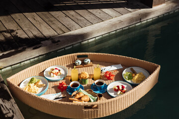 Breakfast in swimming pool, floating breakfast set in tray in resort. Set of floating breakfast tray in swimming pool with fried egg omelette, fruit, juices, sausage, ham, bread and other.