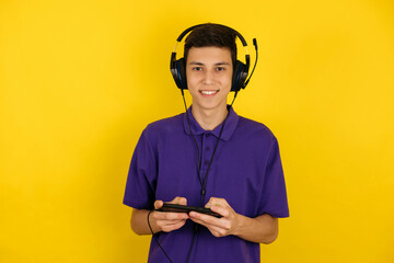 Young guy in headphones and with a phone on a yellow background, listens to music, communicates online with friends
