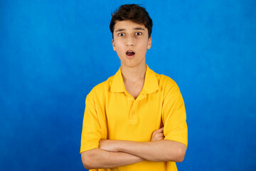 A young man, a teenager, wearing a yellow T-shirt on a blue background with a surprised face