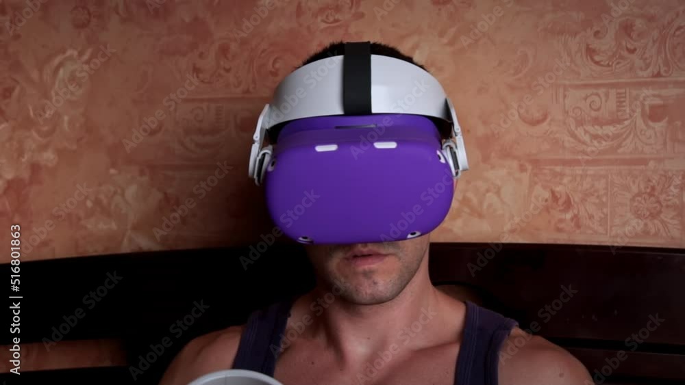 Poster man in a virtual reality helmet controls the controllers. a young man at home sitting on a bed is in
