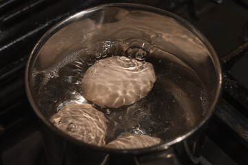 Close-up with boiling eggs in a metal pan, bubbles and steam when boiling water with chicken eggs. Quick breakfast
