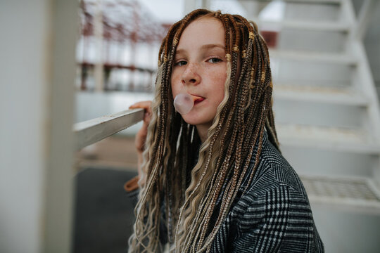 Portrait of a freckled teenager girl with dreads making a gum bubble