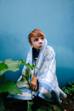unhappy child boy covered himself with a blanket in the yard