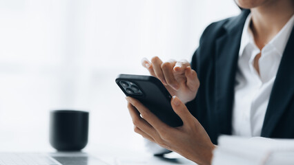 Businesswoman looking at financial information from a mobile phone, she is checking company financial documents, she is a female executive of a startup company. Concept of financial management.