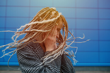 Dreads shaking lighthearted teenage girl in front of a blue panel wall covering.