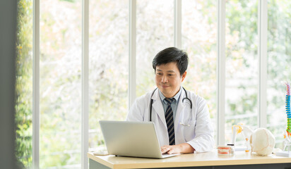 Asian doctor wear uniform with stethoscope sitting in office at the hospital. © amorn