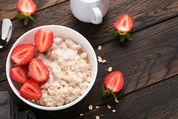 Oatmeal. Bowl of oatmeal porridge with strawberry, almond and milk on old wooden dark table background. Top view in flat lay style. Natural ingredients. Hot and healthy breakfast and diet food.