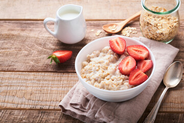Oatmeal. Bowl of oatmeal porridge with strawberry, almond and milk on old wooden dark table background. Top view in flat lay style. Natural ingredients. Hot and healthy breakfast and diet food.