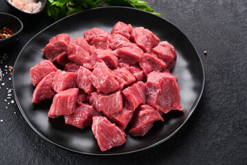 Raw chopped beef meat. Raw organic meat beef or lamb, spices, herbs on black plate on dark grey concrete background. Goulash. Raw uncooked meat. Meat with blood. Top view with copy space.