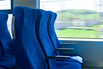 interior of commuter passenger train car, row of chairs and a motion-blurred landscape outside the...