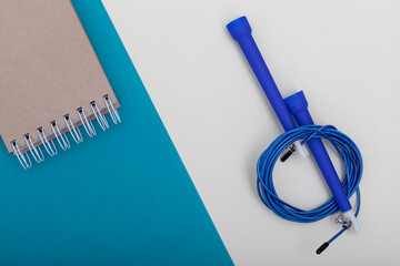 Top view on blue skipping rope and notepad on bicolour surface in a planning for weight losing...