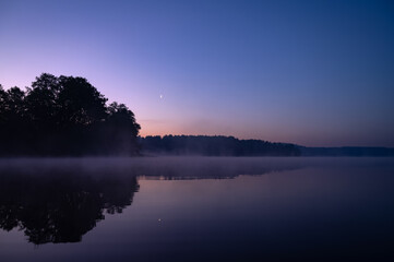 Fototapeta premium Beautiful mystical landscape. Forest lake at summer night before sunrise. Fog above calm water. Scenic nature.