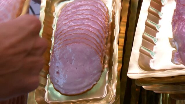 Many packagings of beautiful cold cuts hanging in a row and a man's hand taks one