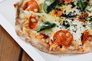 Fresh baked pizza with melted cheese, Italian herbs and tomato sauce and fresh basil on a white plate on a kitchen background, selective focus