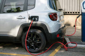 electric car being recharged, connected with the red cable to the electrical control unit, where it...