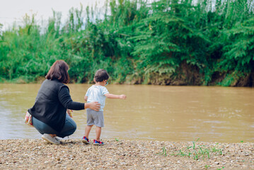 A mother watching over her child stands watching the river on the beach.