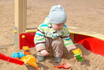 A little boy is playing in a children's sandbox with plastic toys. Kids playing on the playground